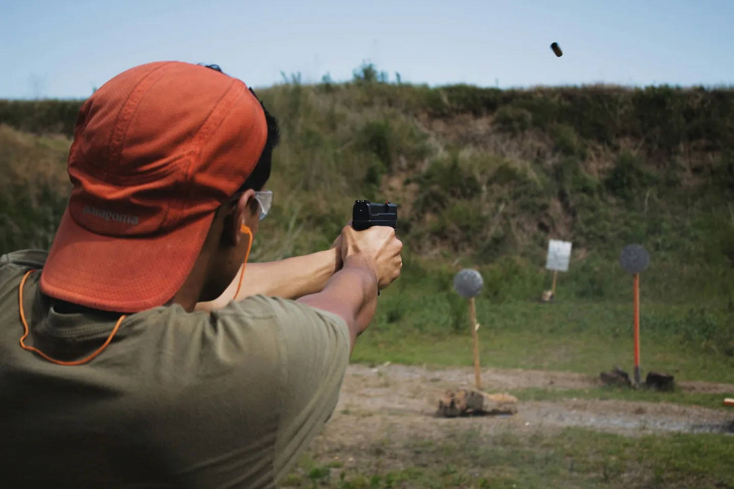 Shooter wearing eye and hearing protection firing a handgun at an outdoor range